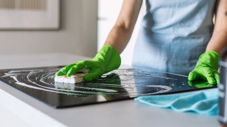 Hands wiping down a glass cooktop.