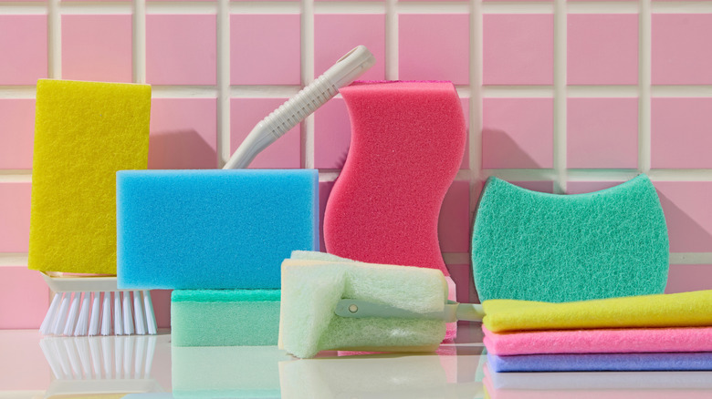 Kitchen sponges, brushes, and clothes in front of pink tile