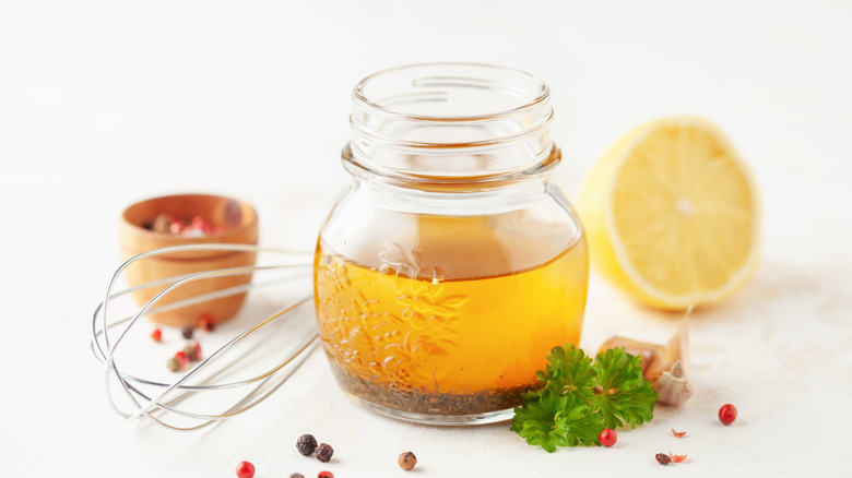 small jar of separated vinaigrette with whisk, lemon, pepper