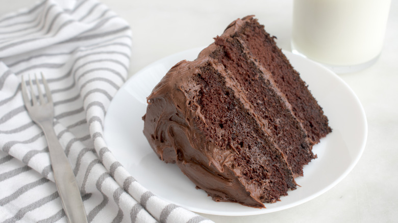 Large slice of chocolate cake on white plate next to fork and napkin