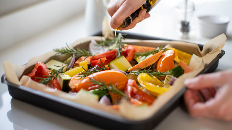 Person preparing tray of vegetables for roasting by sprinkling olive oil on top.