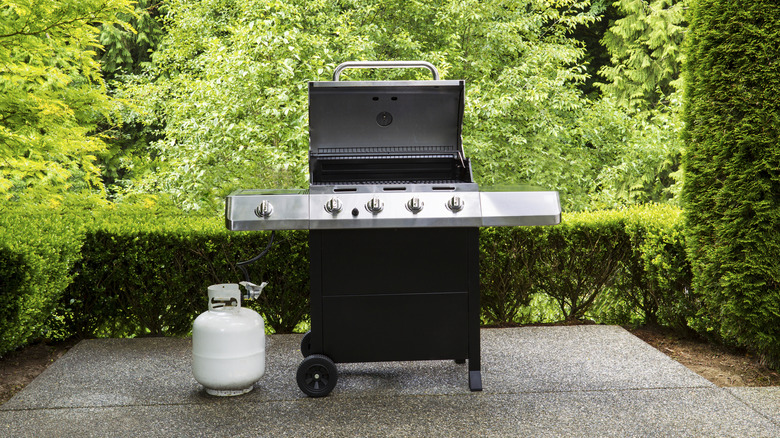 An open gaas grill rests on an outdoor patio against a background of greenery