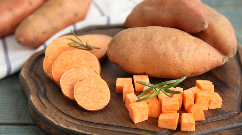 Wooden board with cut and whole sweet potatoes on table