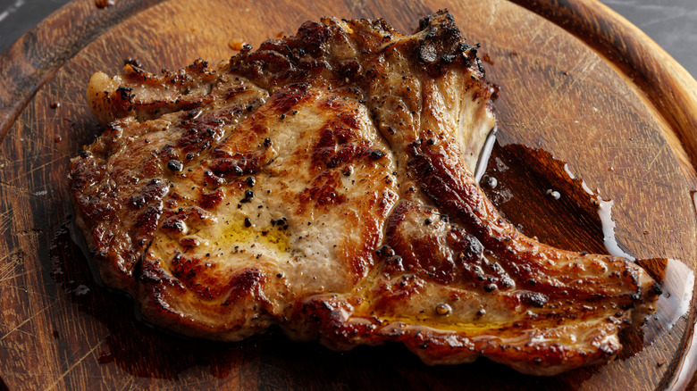 A grilled pork chop on a wooden platter