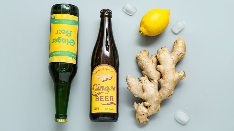 bottles of ginger beer next to a ginger root, ice cubes, and a lemon