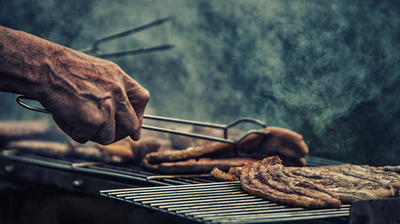 A man flips over a piece of pork belly on the grill