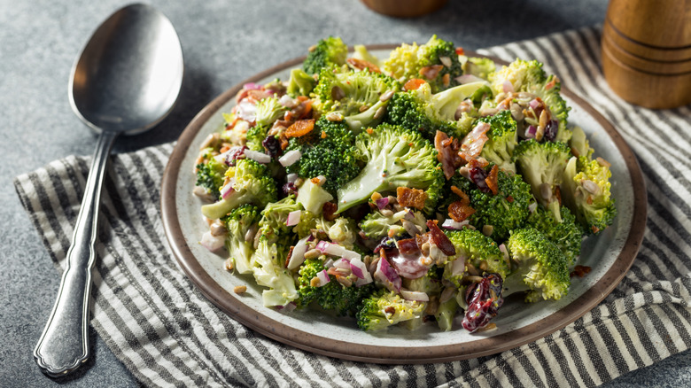 A plate of raw broccoli salad with onions and bacon with a spoon