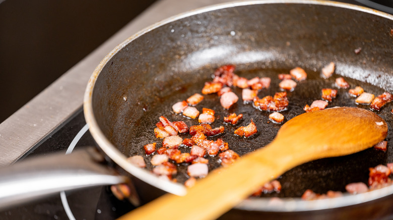 Frying pan with sauteed chopped bacon and a wooden spoon