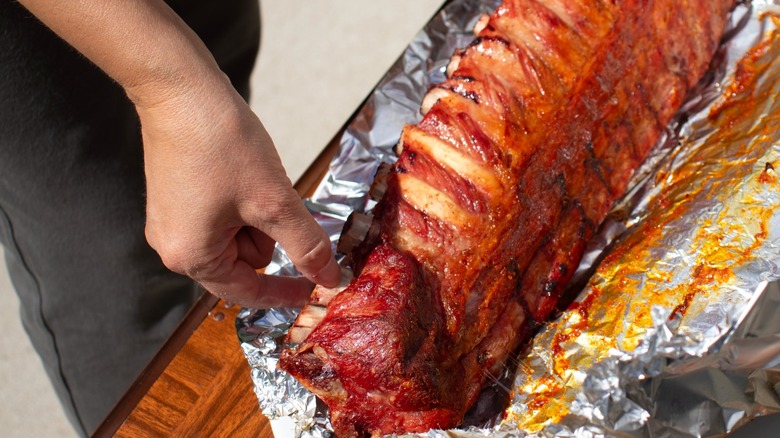 Person lifting cooked ribs from foil