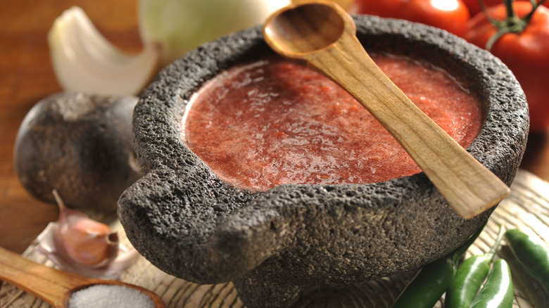 Red salsa in a volcanic rock bowl with a wooden spoon