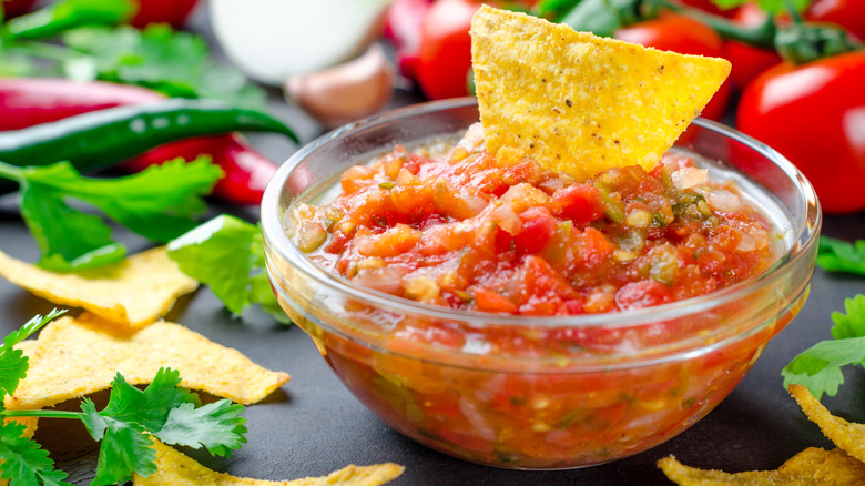 A small bowl of red salsa with a tortilla chip