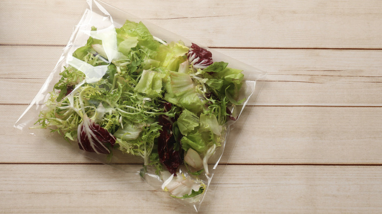 Sealed plastic bag filled with greens inside on wooden surface