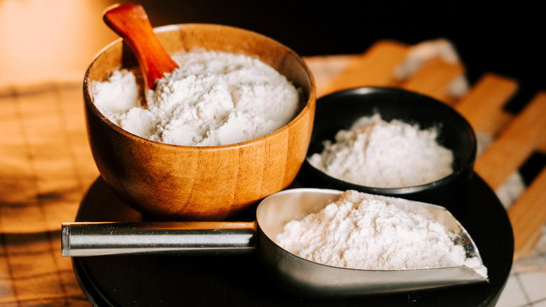 Flour in a wooden bowl with a scoop of flour lying in front.
