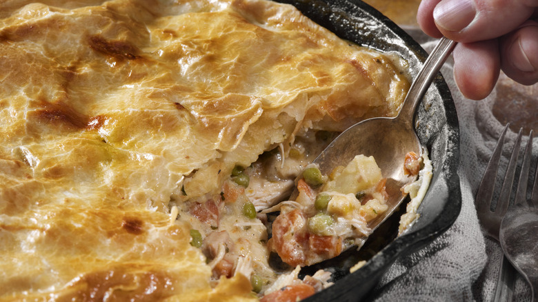 A cast iron skillet of chicken pot pie, with a spoon removing a bite