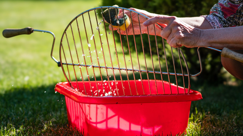 A person cleans a grate from a grill in a bucket of water