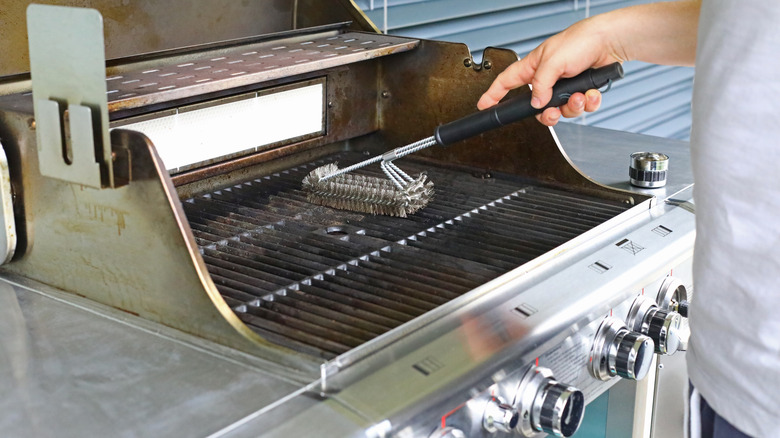 A person scrubs grill grates with a wire brush