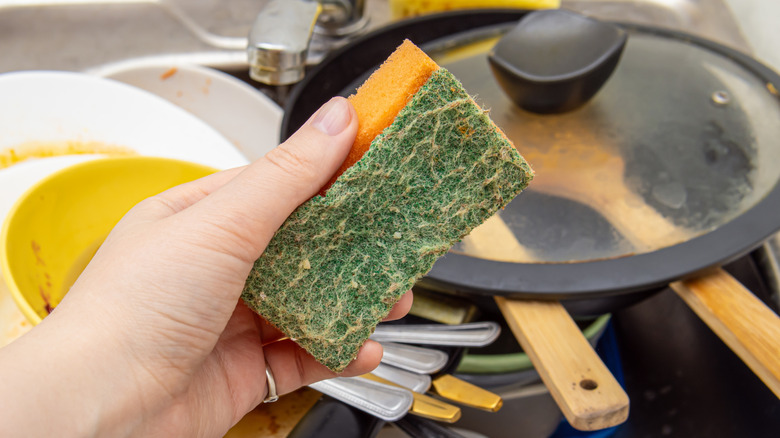 hands hold dirty kitchen sponge in front of dishes