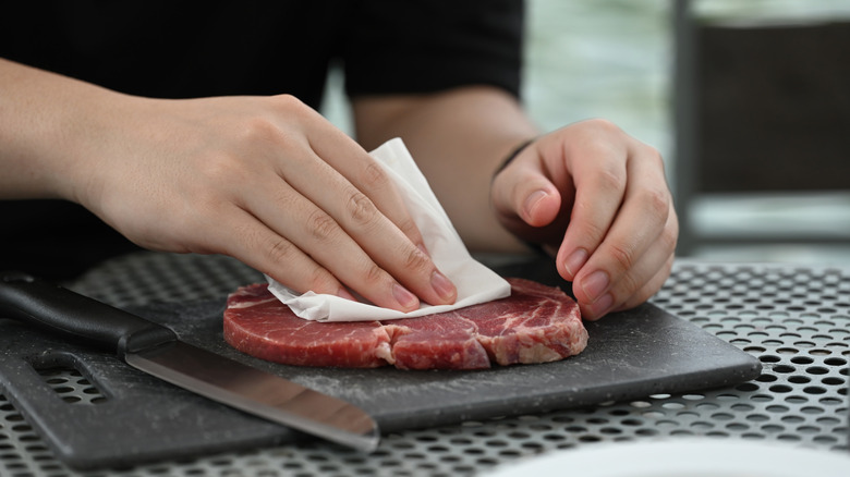 person uses paper towel to dry off raw steak