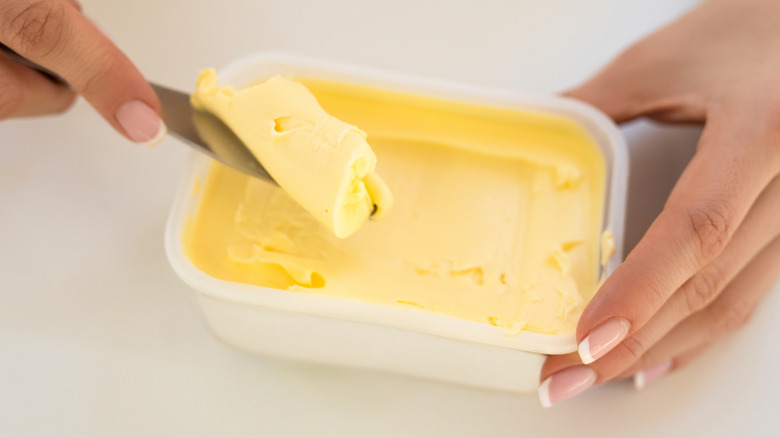 Hand using knife to scoop out spreadable butter from white container