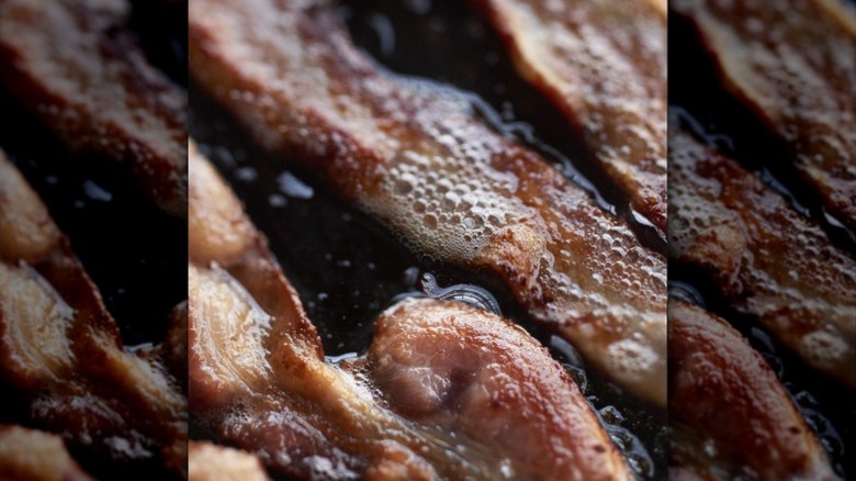 Close up of grease bubbling up on strips of bacon in a pot or pan.