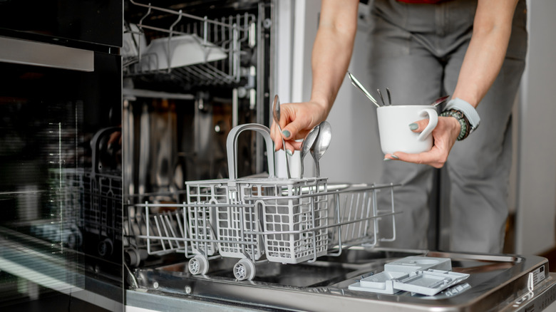 Someone loading spoons into a dishwasher.