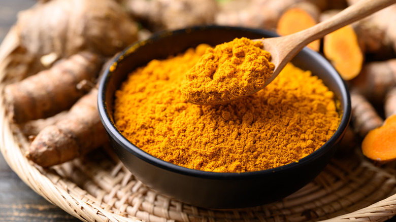 turmeric roots surrounding a bowl of powdered turmeric on a woven plate